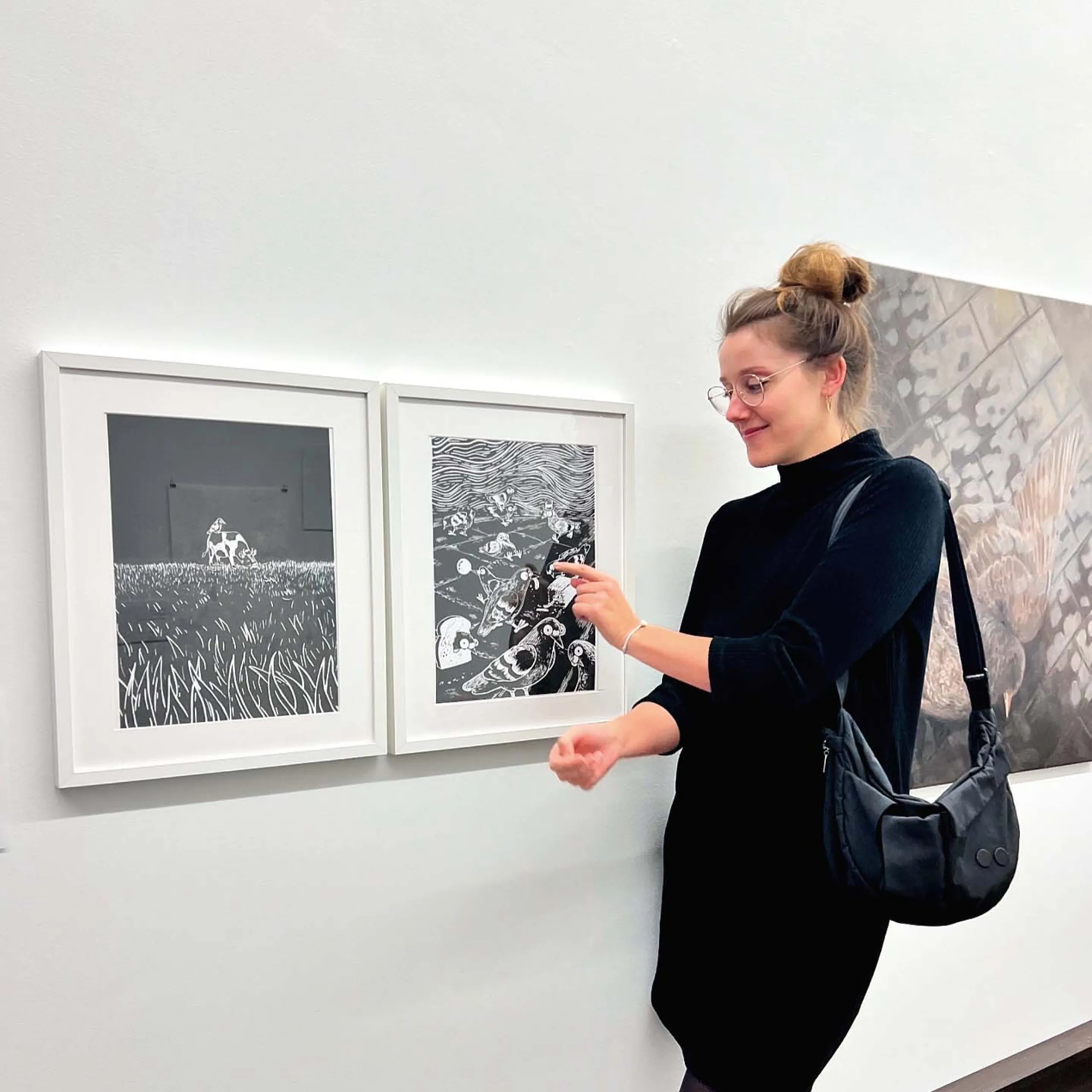 Fotografie der Künstlerin in schwarzem Kleid, die vor einer Ausstellung ihrer Linoldrucke steht.