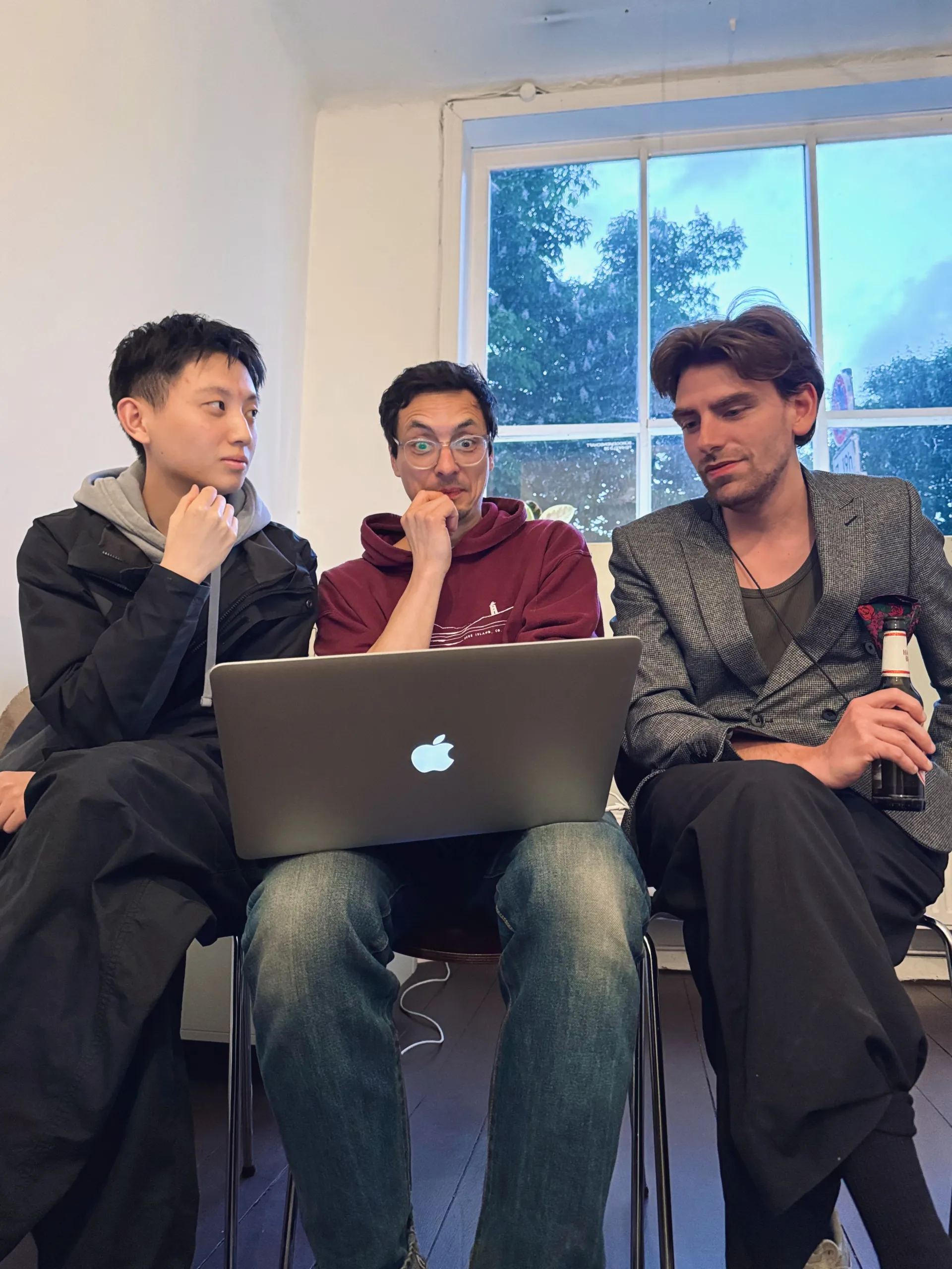 Drei Typen schauen auf einen Laptop, den der mittlere Typ auf dem Schoß hat.